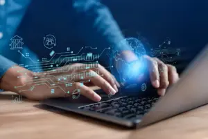 Hands of a man typing on the keyboard with technology icons in the shape of holograms floating above it.